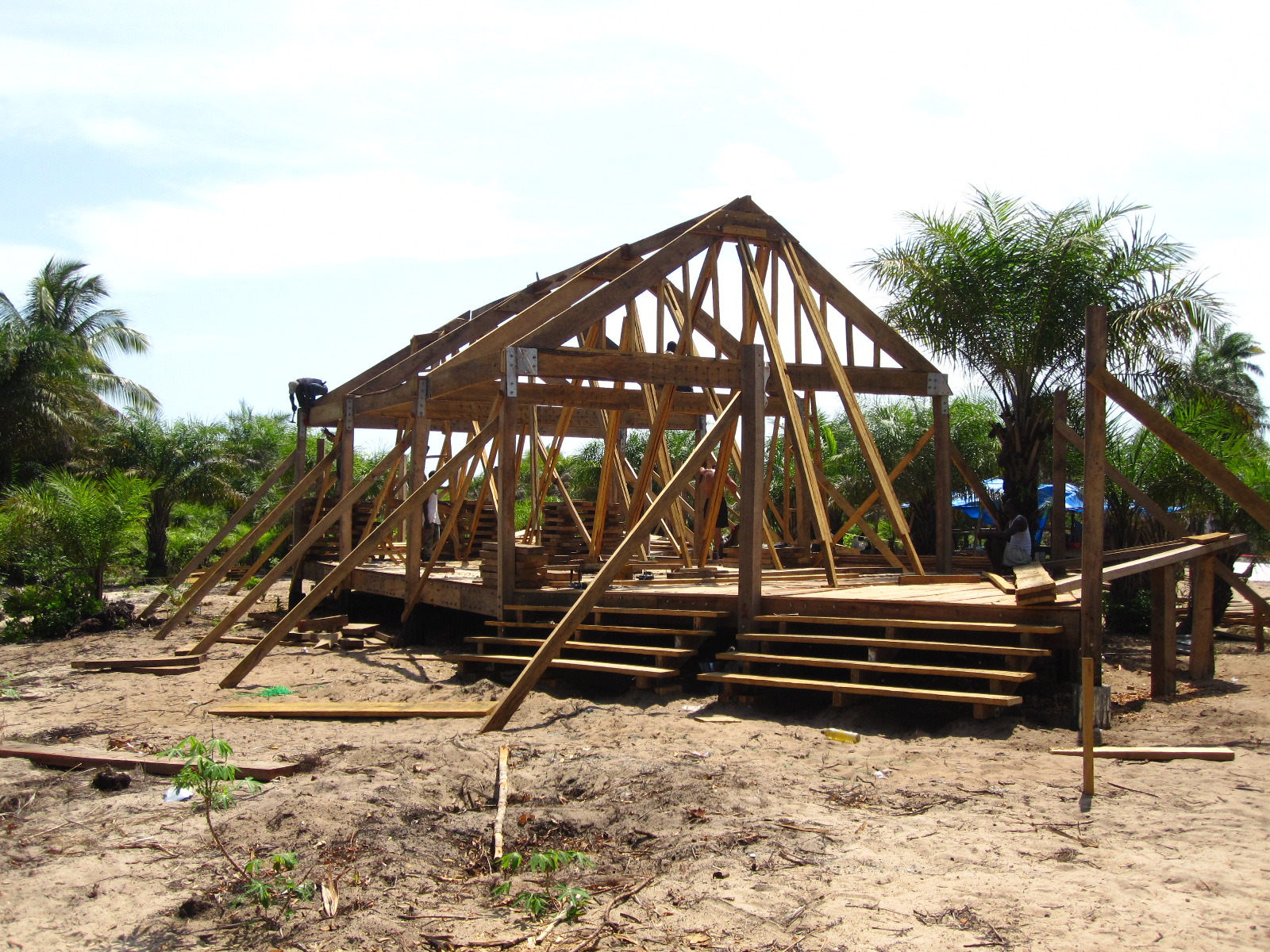 A timber building frame stands on a raised platform with wide entrance steps and diagonal bracing.