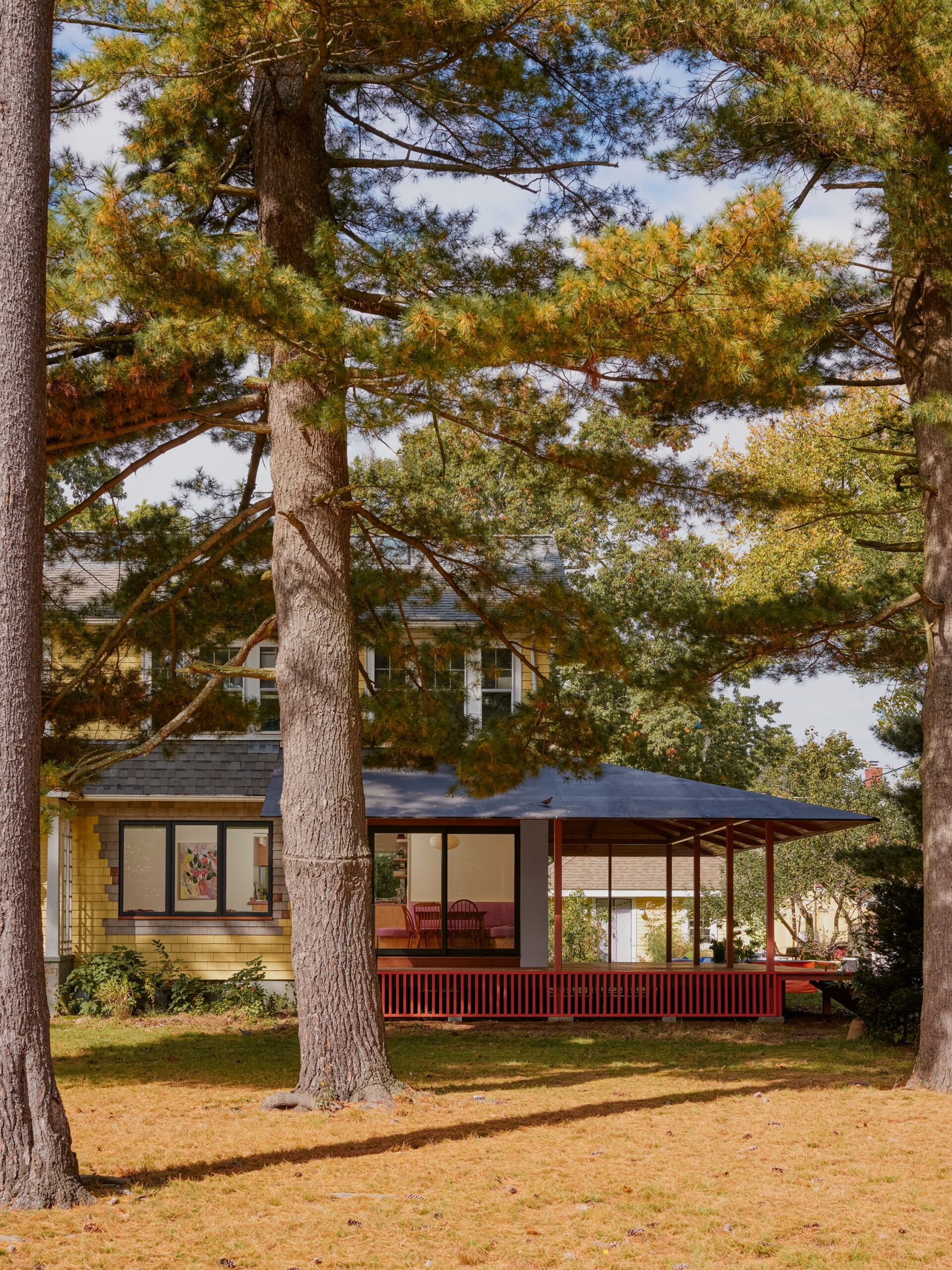 Small glazed pavilion with a covered porch beneath large trees.