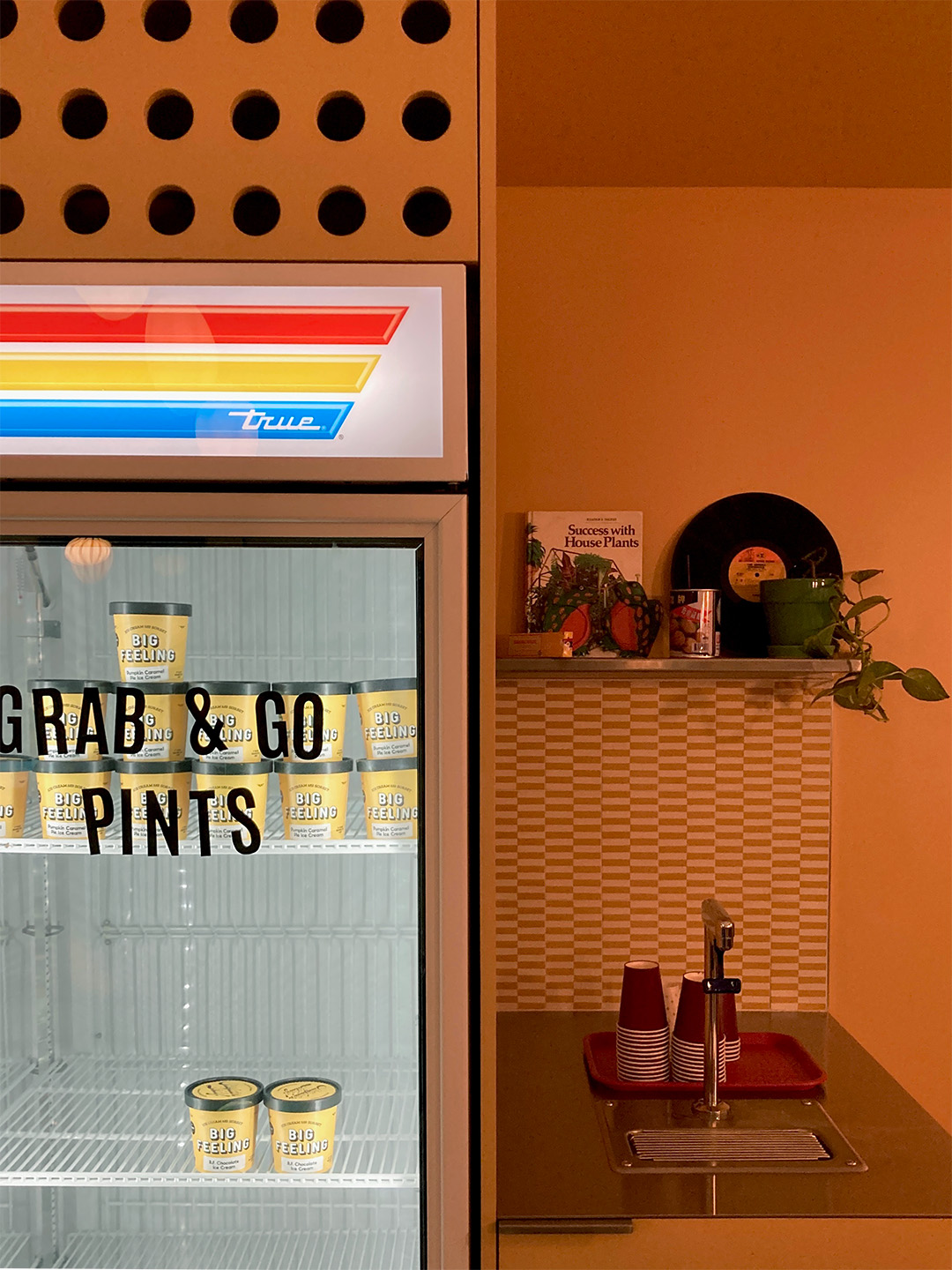 Glass-front freezer labeled Grab & Go Pints beside an orange alcove with a small sink.