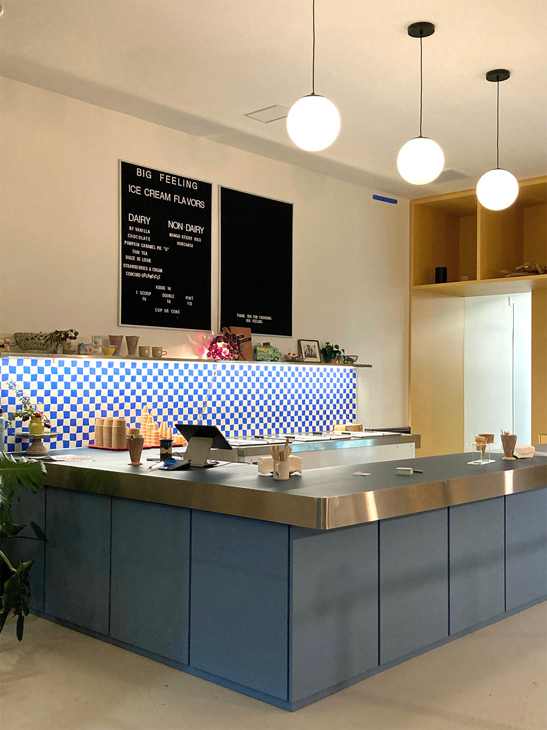 Ice cream shop counter with blue cabinets, checkerboard tile, menu boards and globe pendant lights.