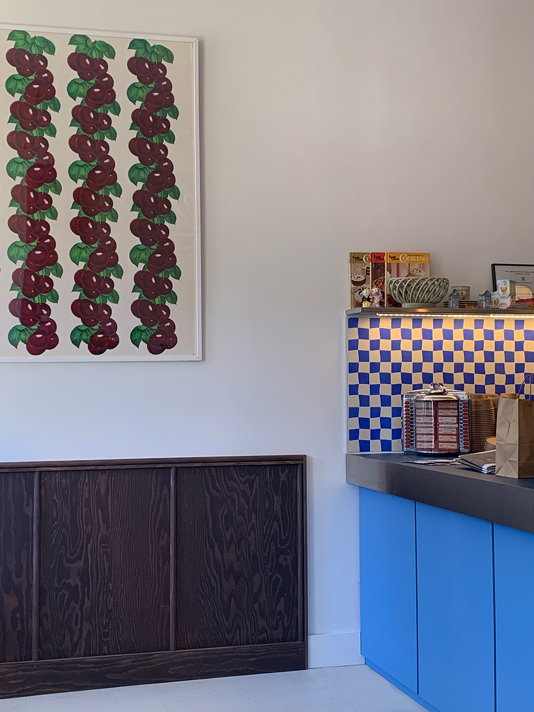Blue cabinetry and a blue-and-yellow checkerboard backsplash beside framed artwork and dark wood paneling.