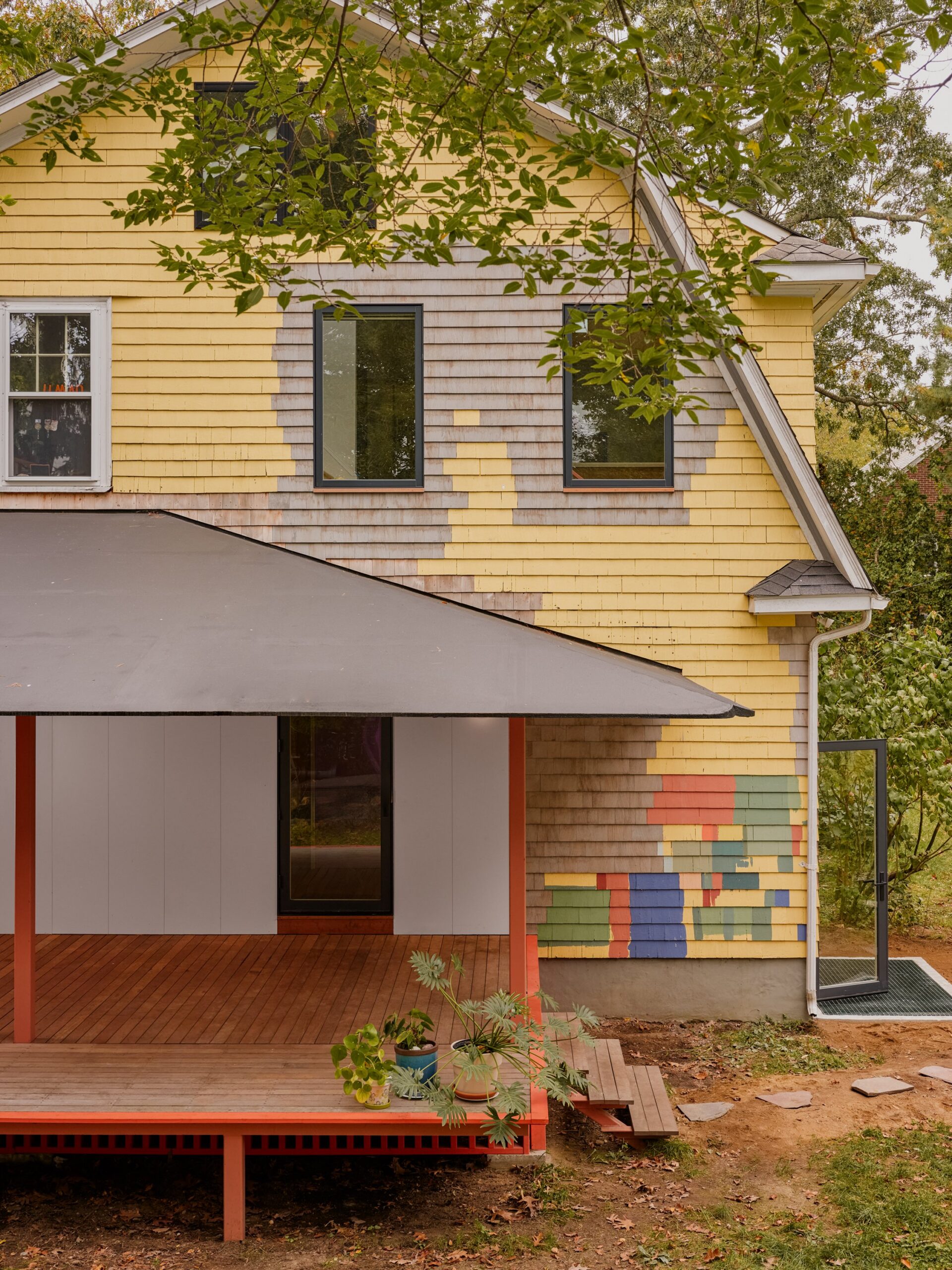 A red-framed porch meets a yellow house with a patchwork of brightly colored siding.