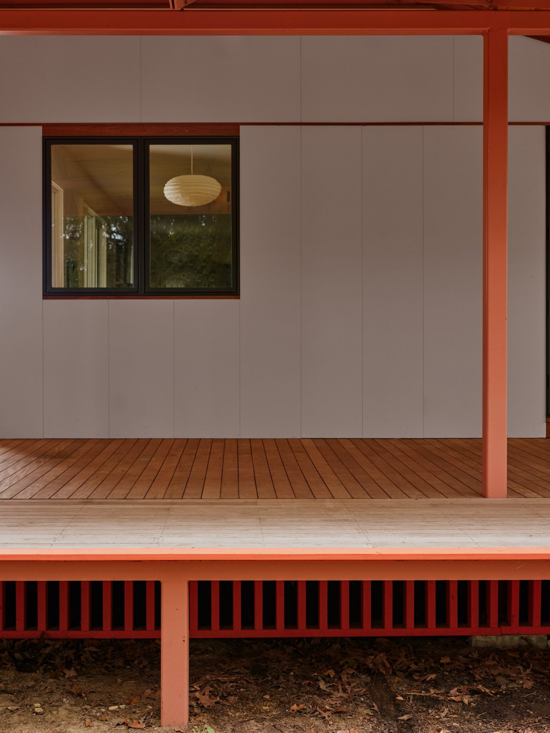 Red porch columns frame a gray wall, black-framed window and timber deck.