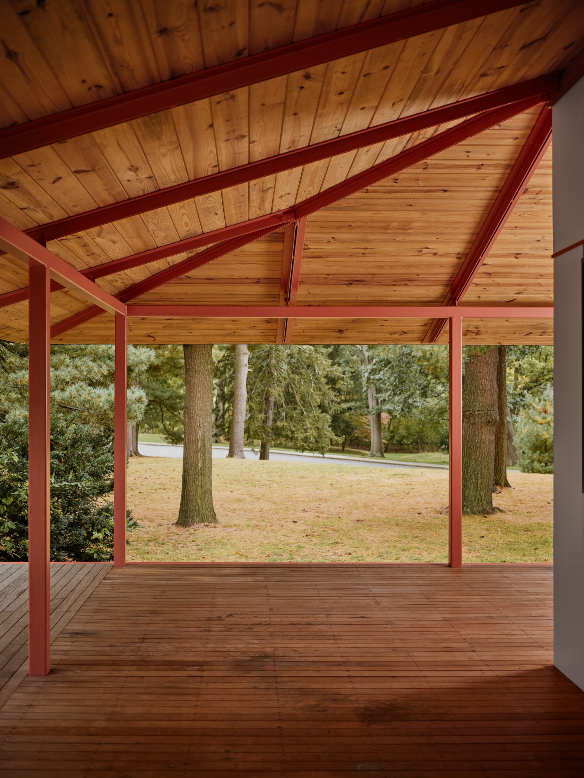Red framing supports a timber-lined porch roof overlooking trees and lawn.