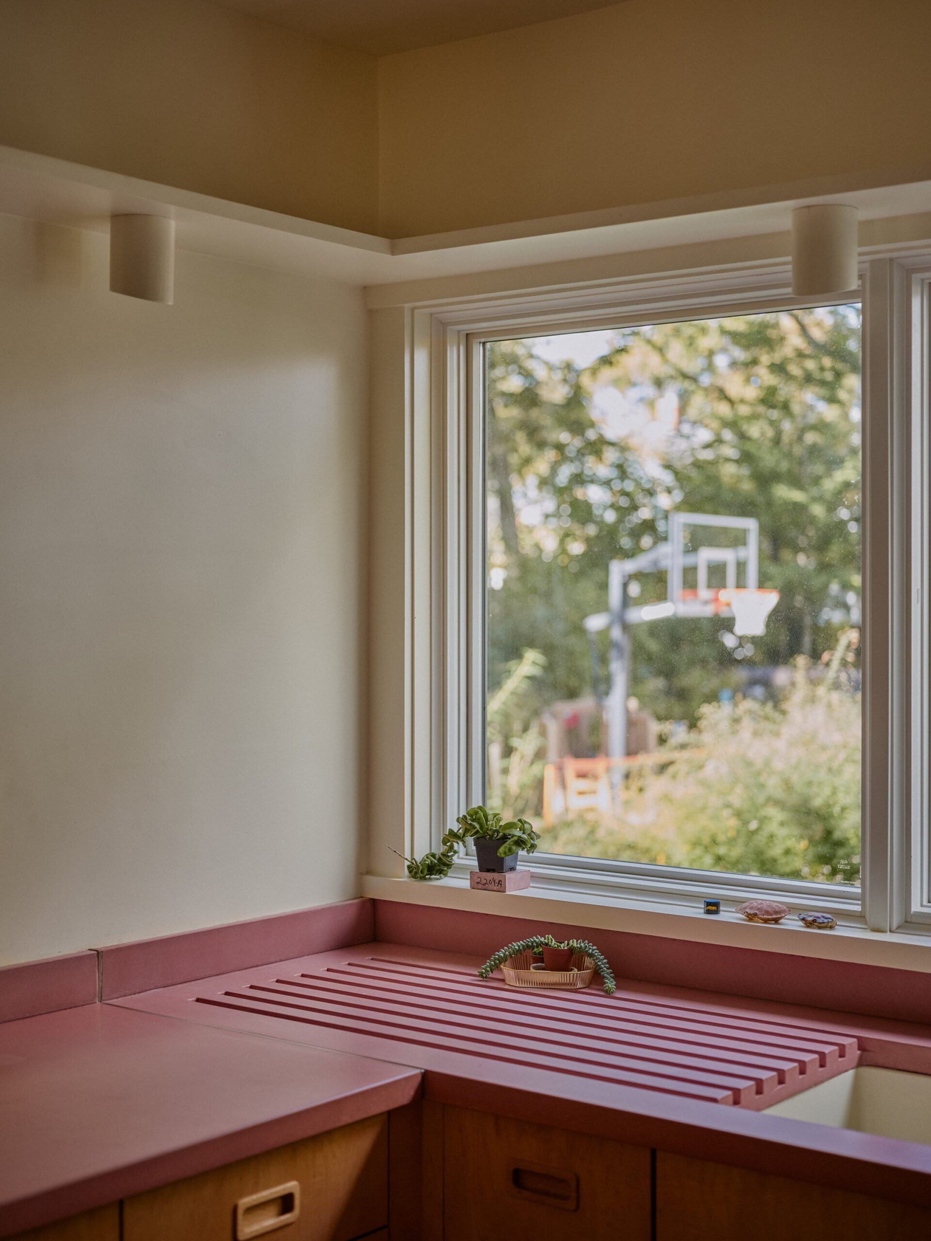 Kitchen corner with wood cabinets, a muted red counter and integrated draining board beneath a large window.