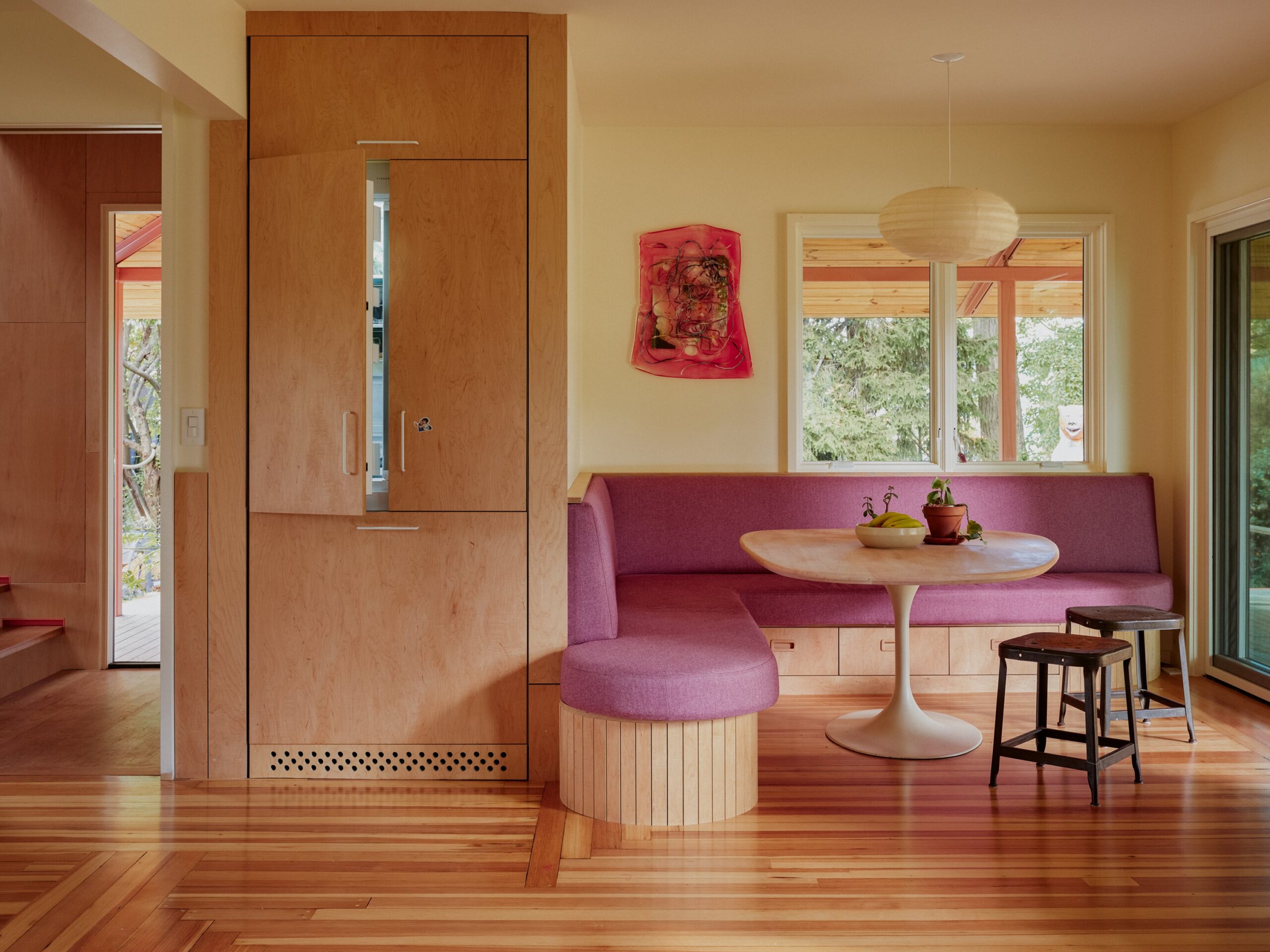 A pink curved banquette and round table sit beside tall wooden cabinetry and a matching rounded seat.