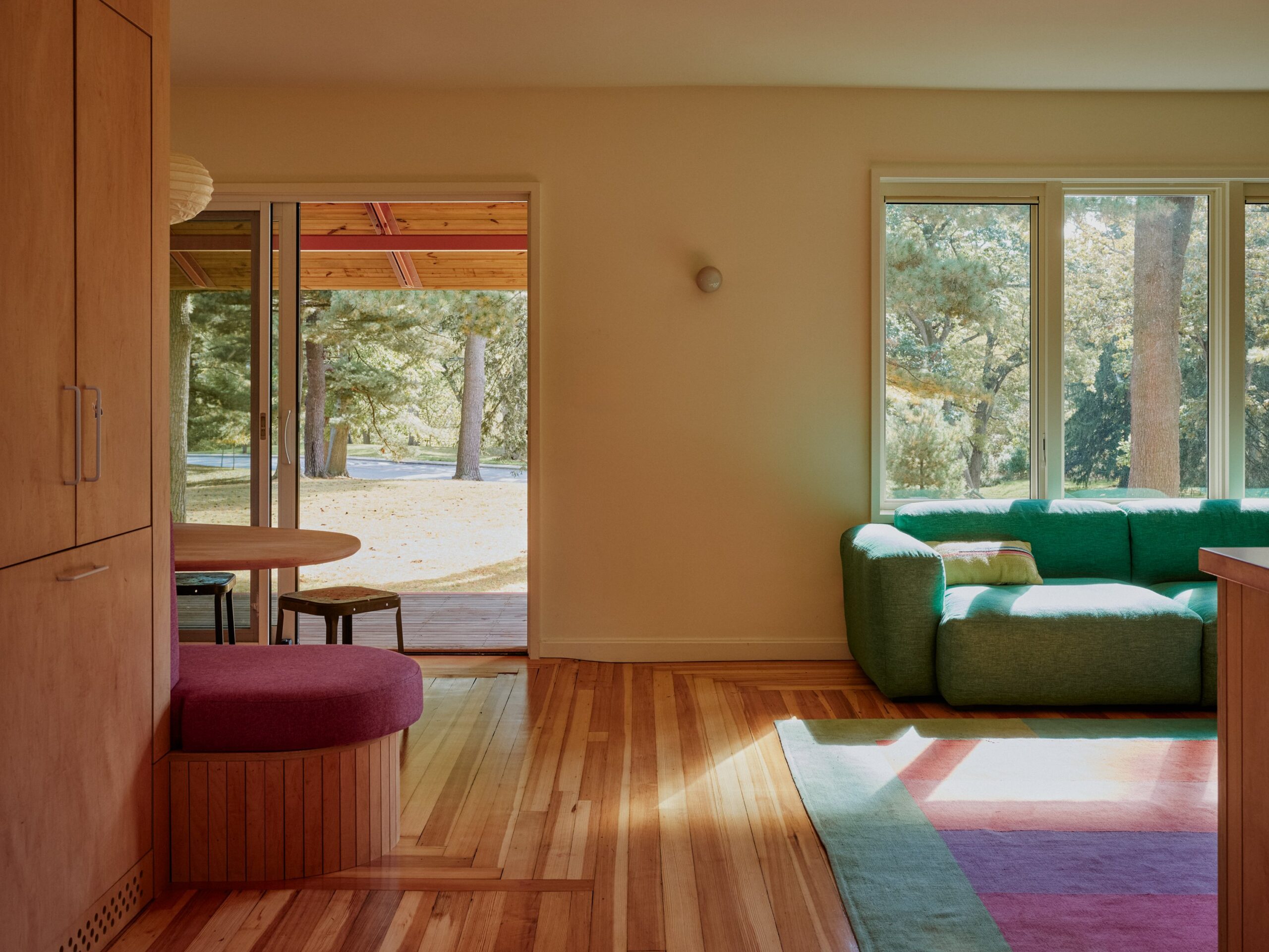A green sofa and curved pink seat face a sunlit living space opening toward a covered porch.