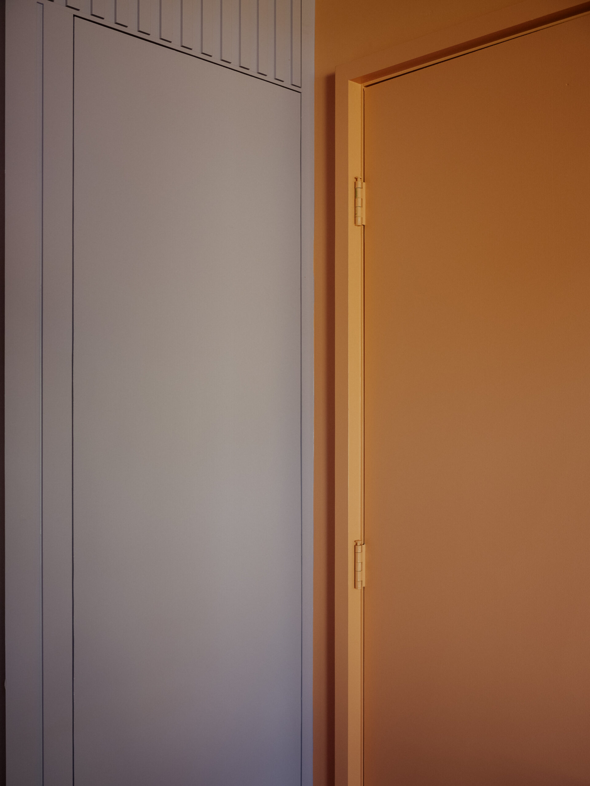 Close-up of a pale paneled wall and doorway opening into an orange room.