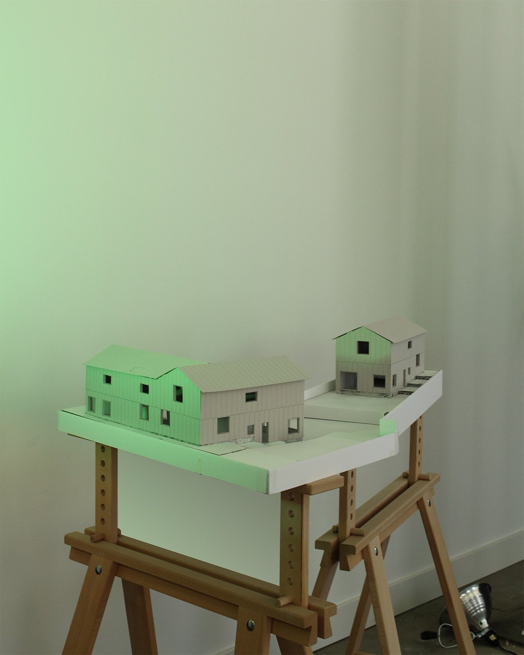 Two white building models occupy an elongated site model supported on wooden trestles.