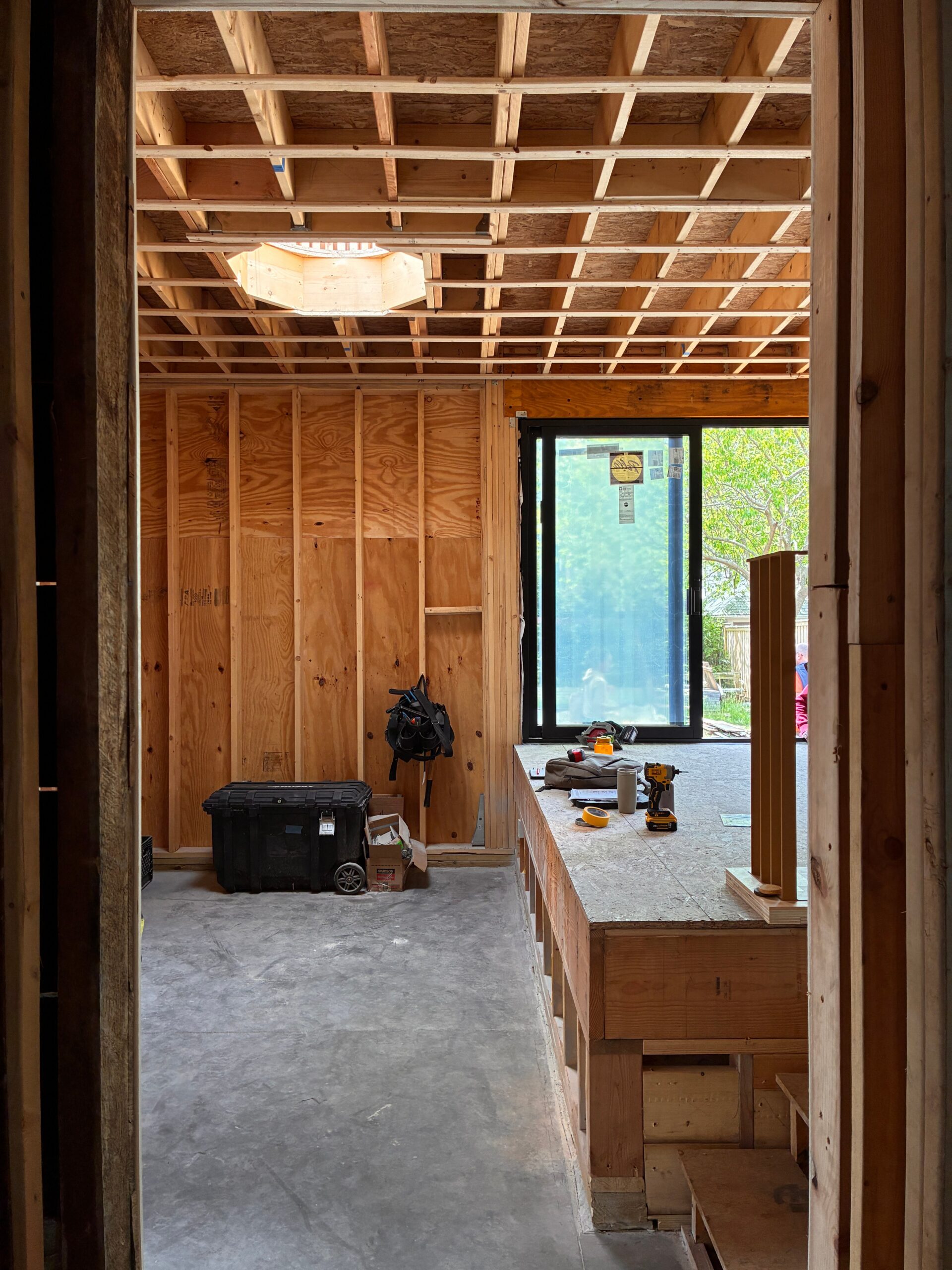 Unfinished addition interior with exposed framing, a roof opening and glazed doors to the garden.