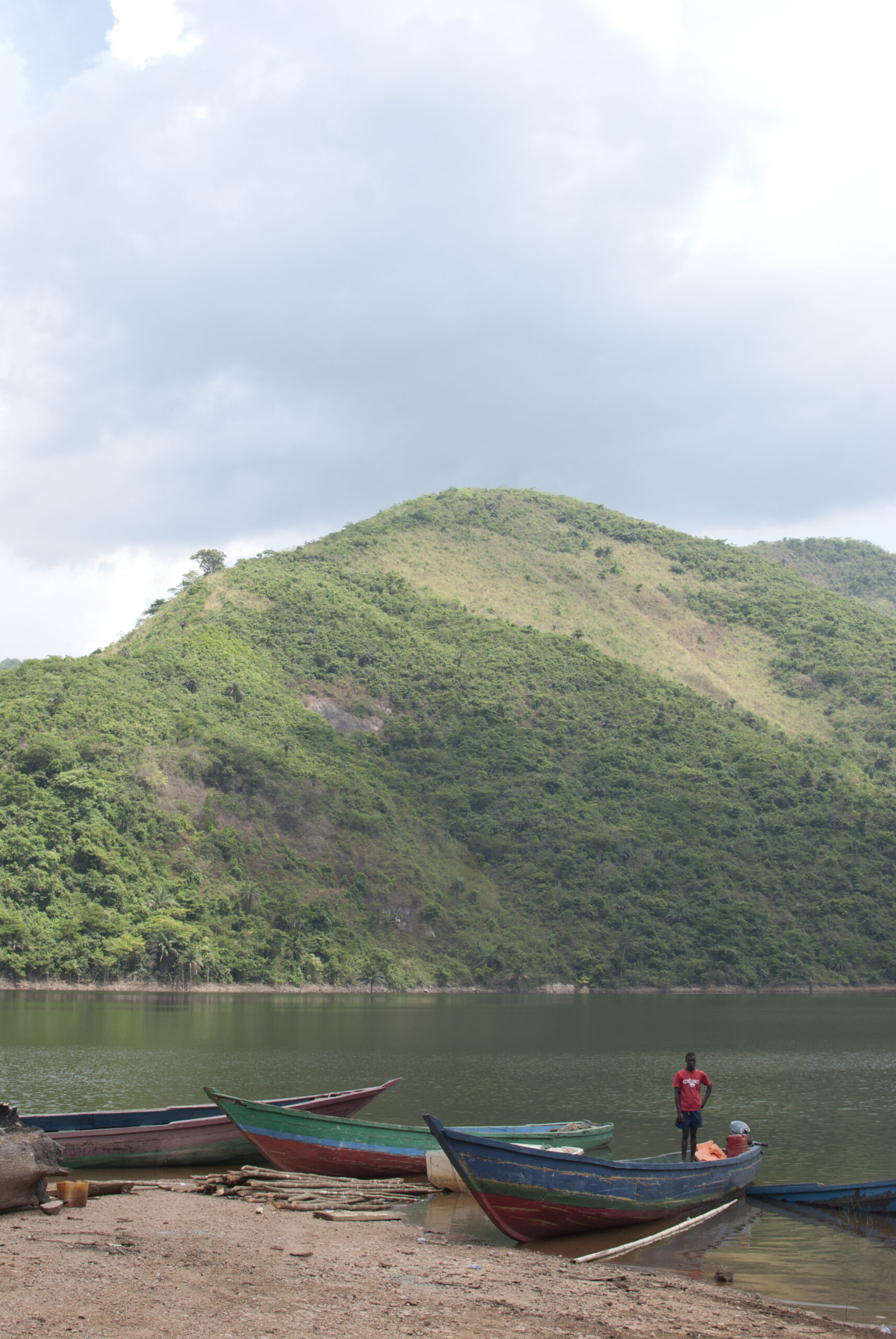 Small boats on a shoreline beneath a green hillside across the water.