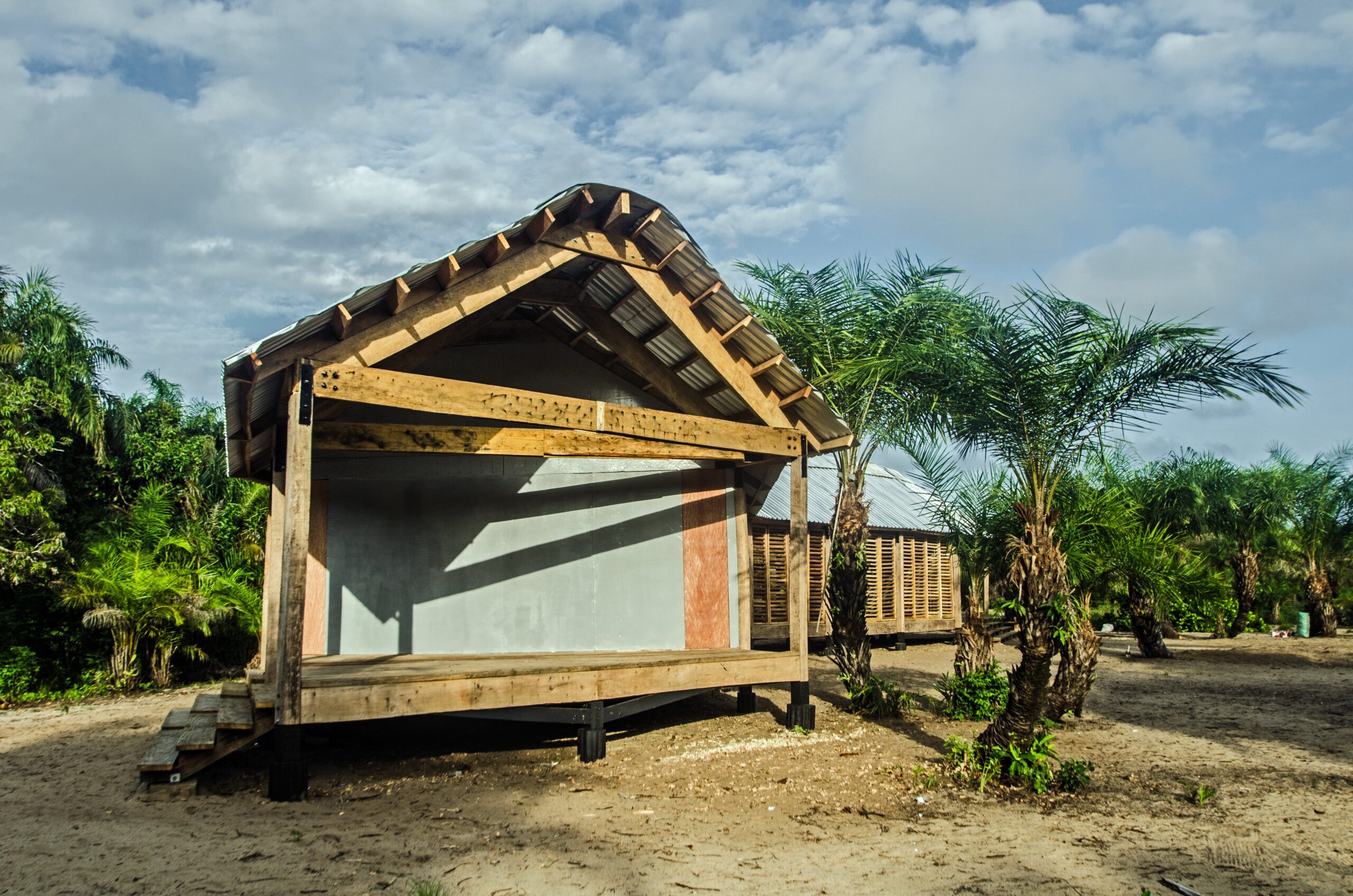 Gabled timber classroom building with an open end, raised floor and surrounding palms.