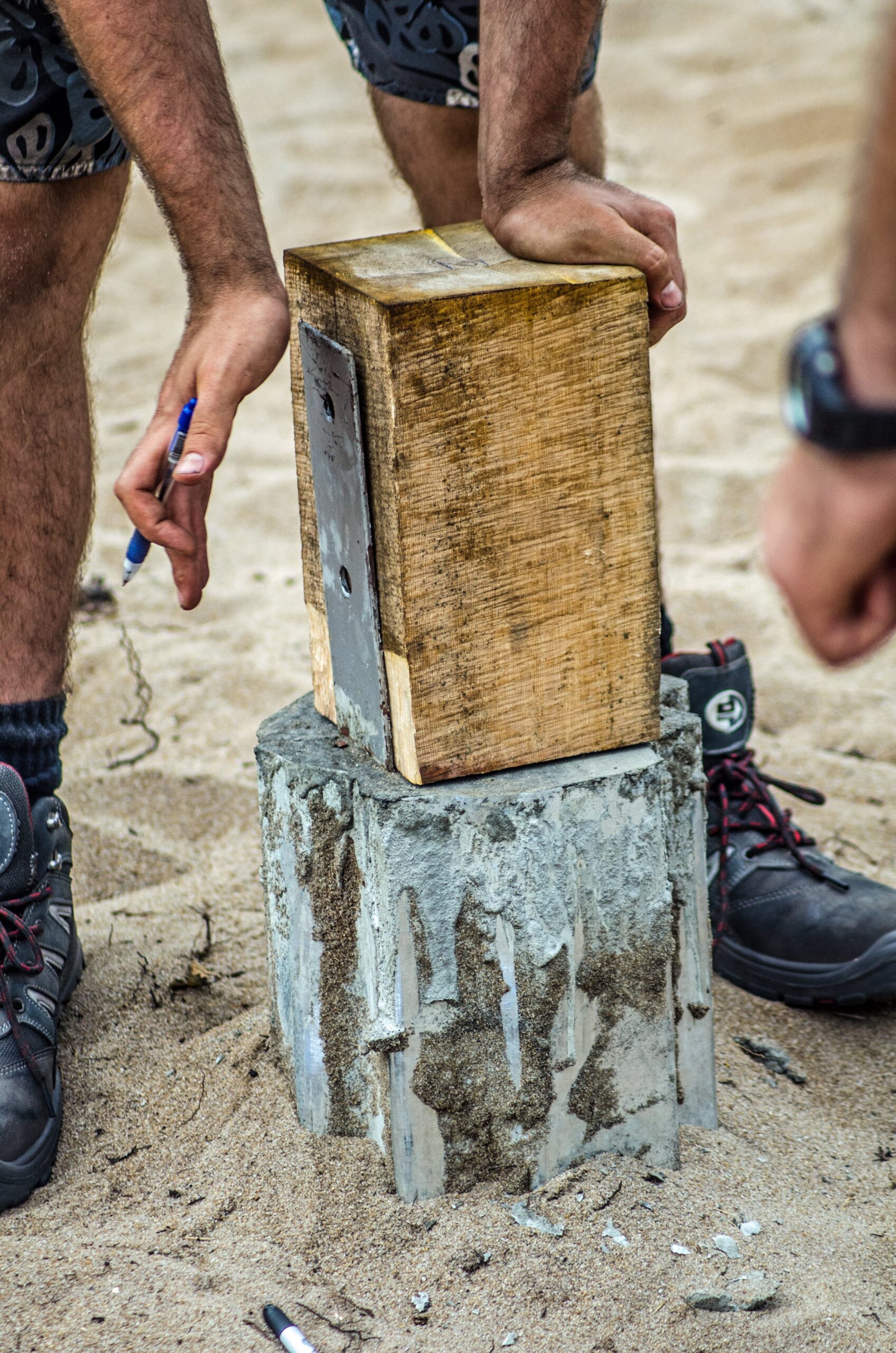 Close-up of hands positioning a timber piece above a concrete support during construction.