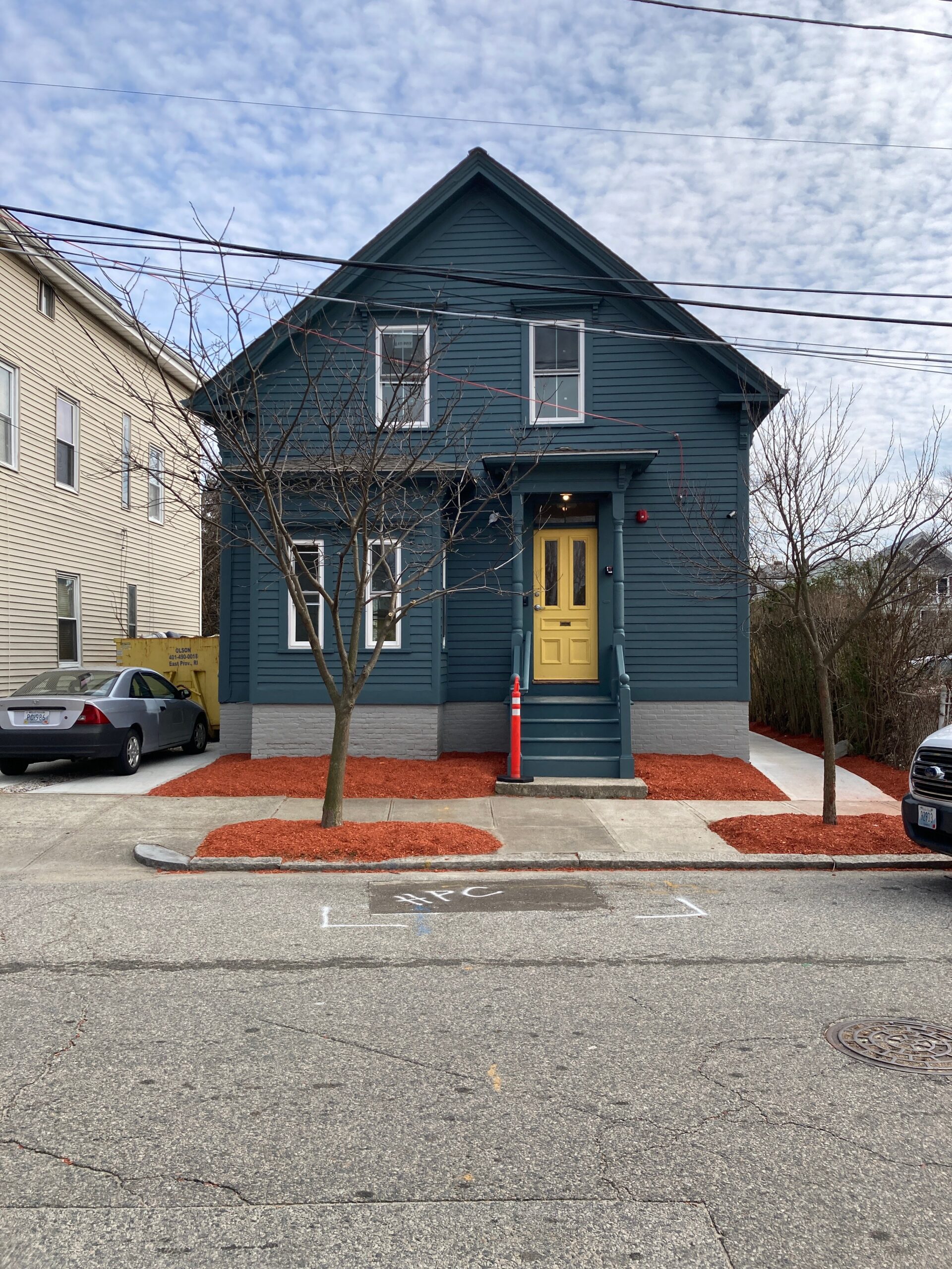Blue two-story school building with a yellow front door, entry steps and red ground cover.