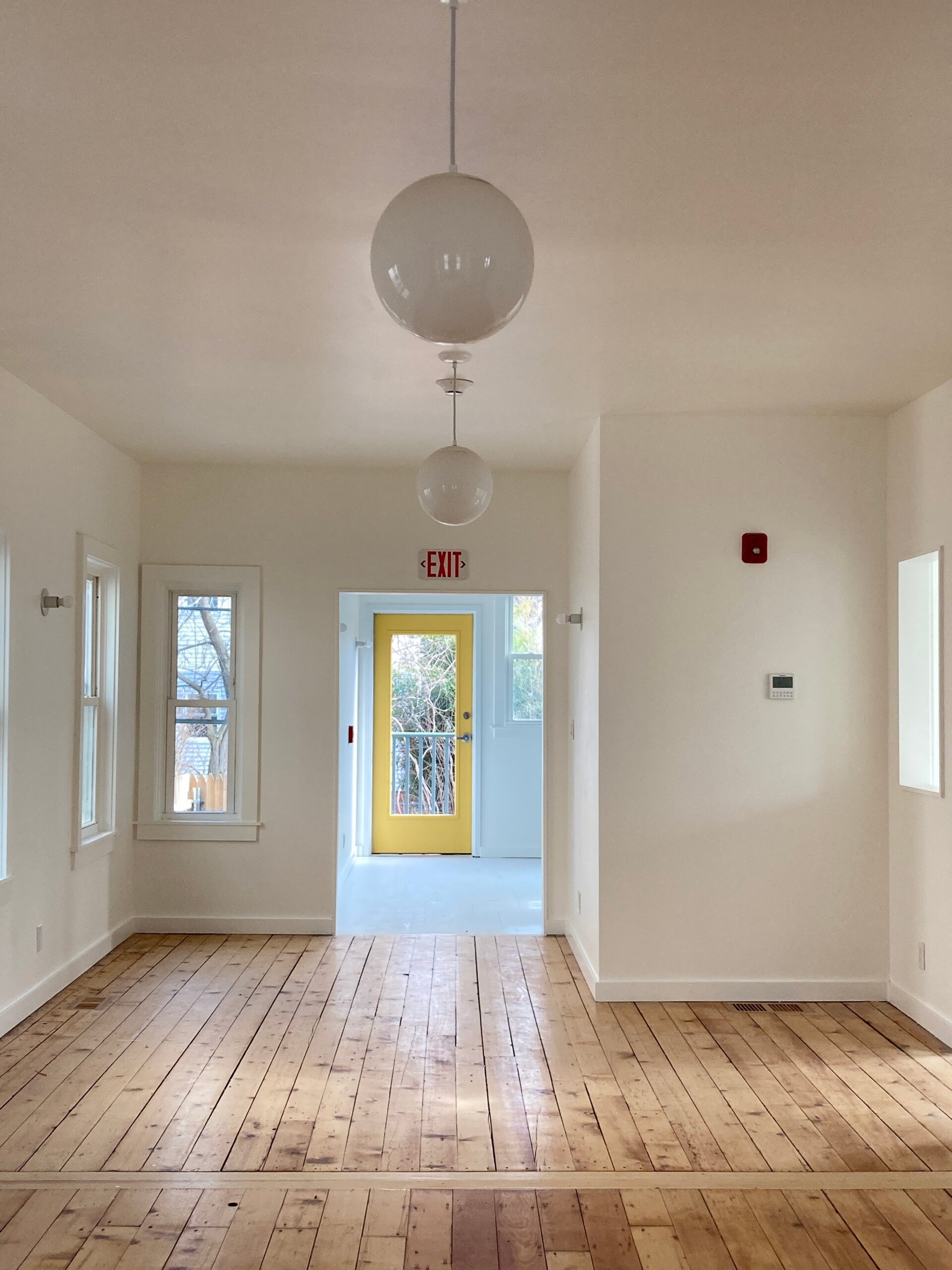 Bright school room with wood flooring, globe pendant lights and a yellow glazed door.
