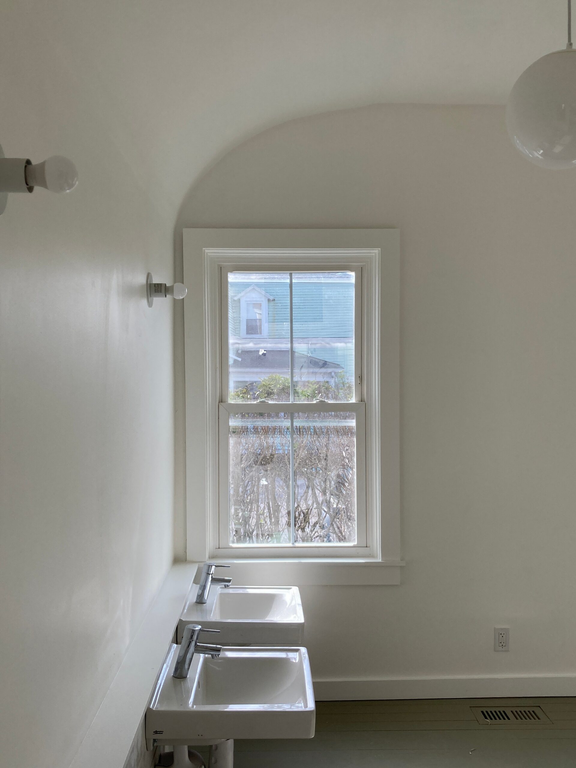 Two small wall-mounted washbasins beneath a window in a white room with an arched ceiling.