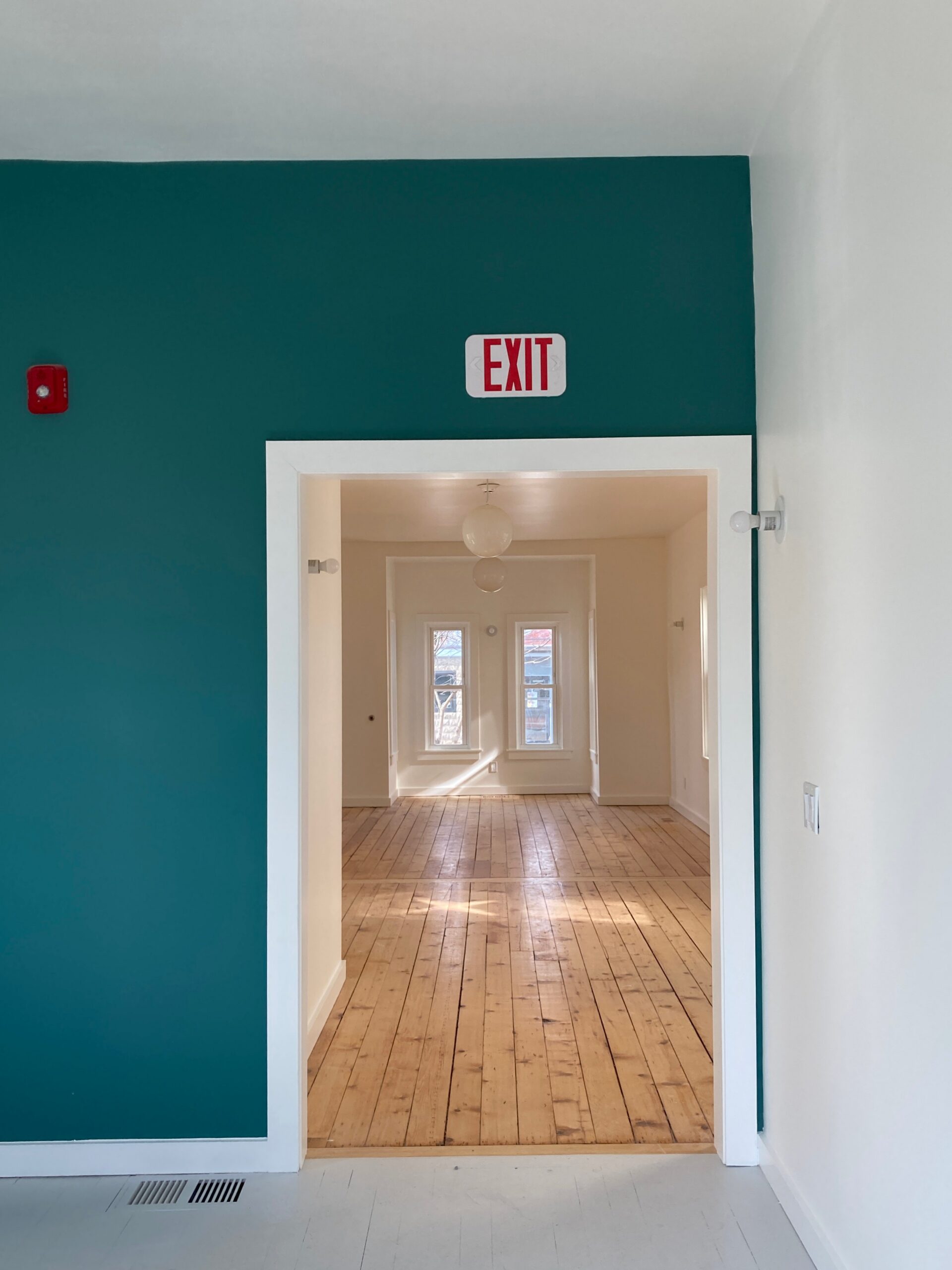 Teal accent wall frames a doorway leading to a wood-floored school room.