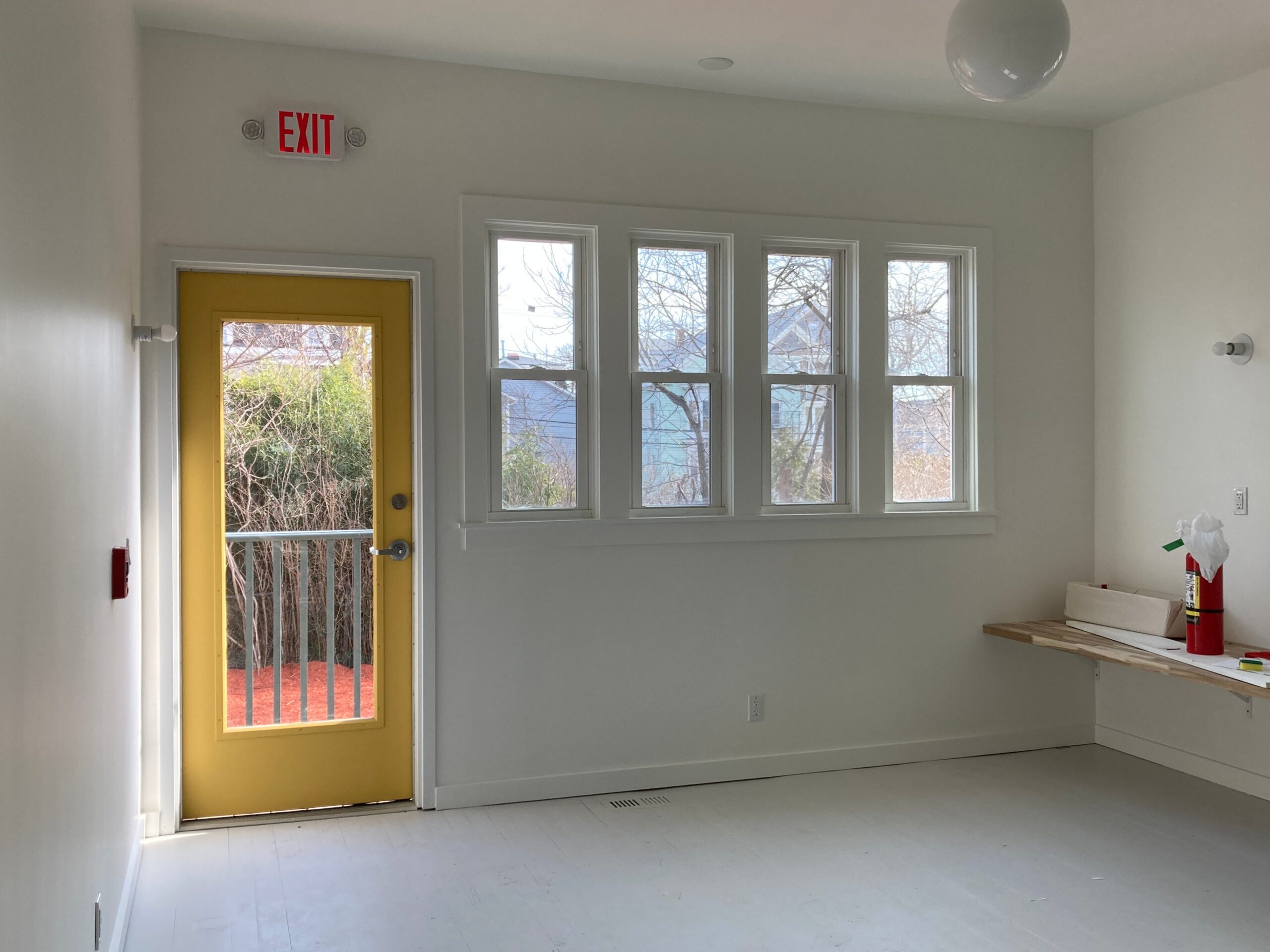 White classroom with a yellow glazed door, three windows and a low counter.