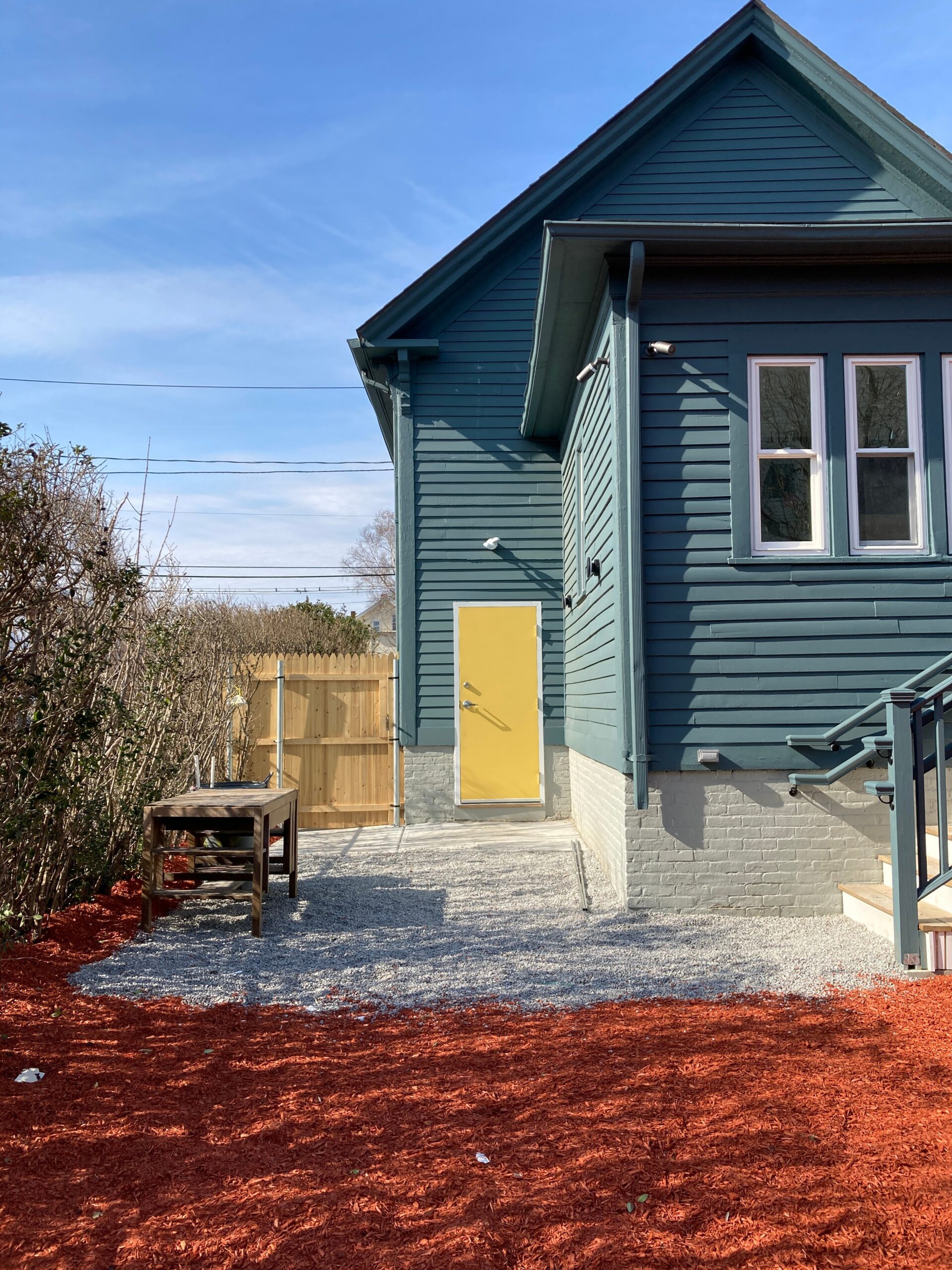 Blue-clad school exterior with a yellow side door, gravel path and red ground cover.