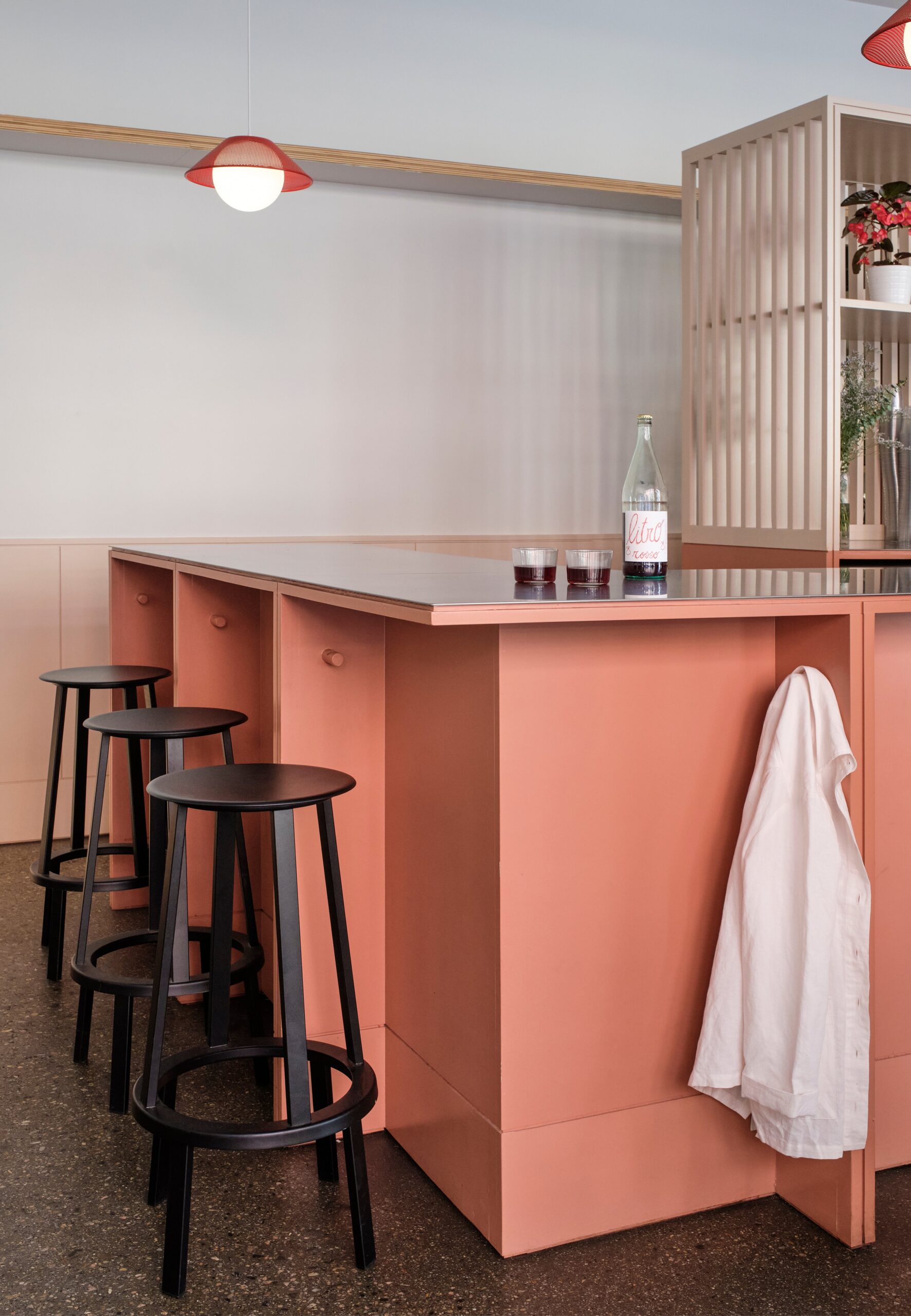 Black stools line a coral-colored café counter beside a vertical slatted screen.