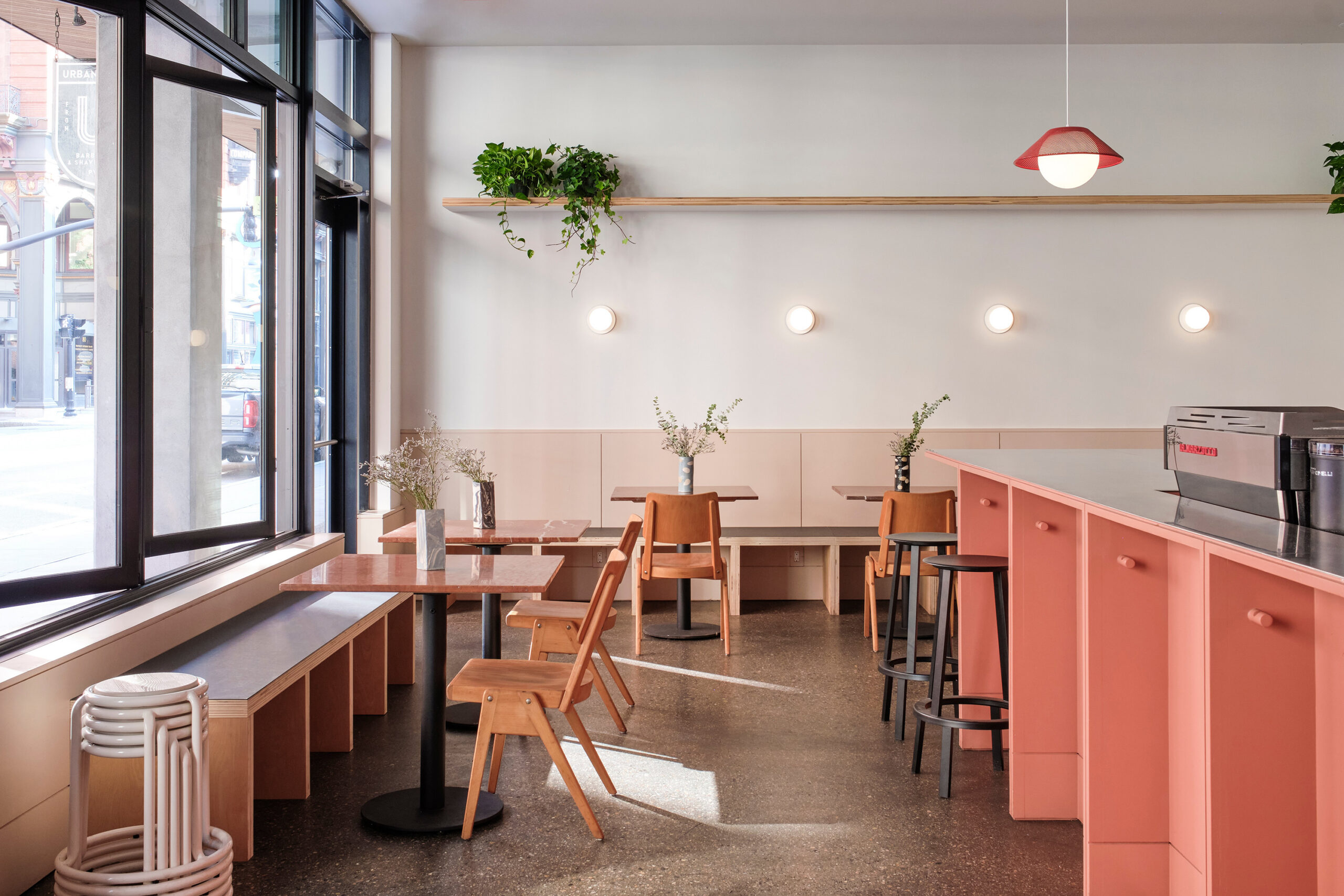 Street-facing windows light café tables, wooden seating and a coral-colored service counter.