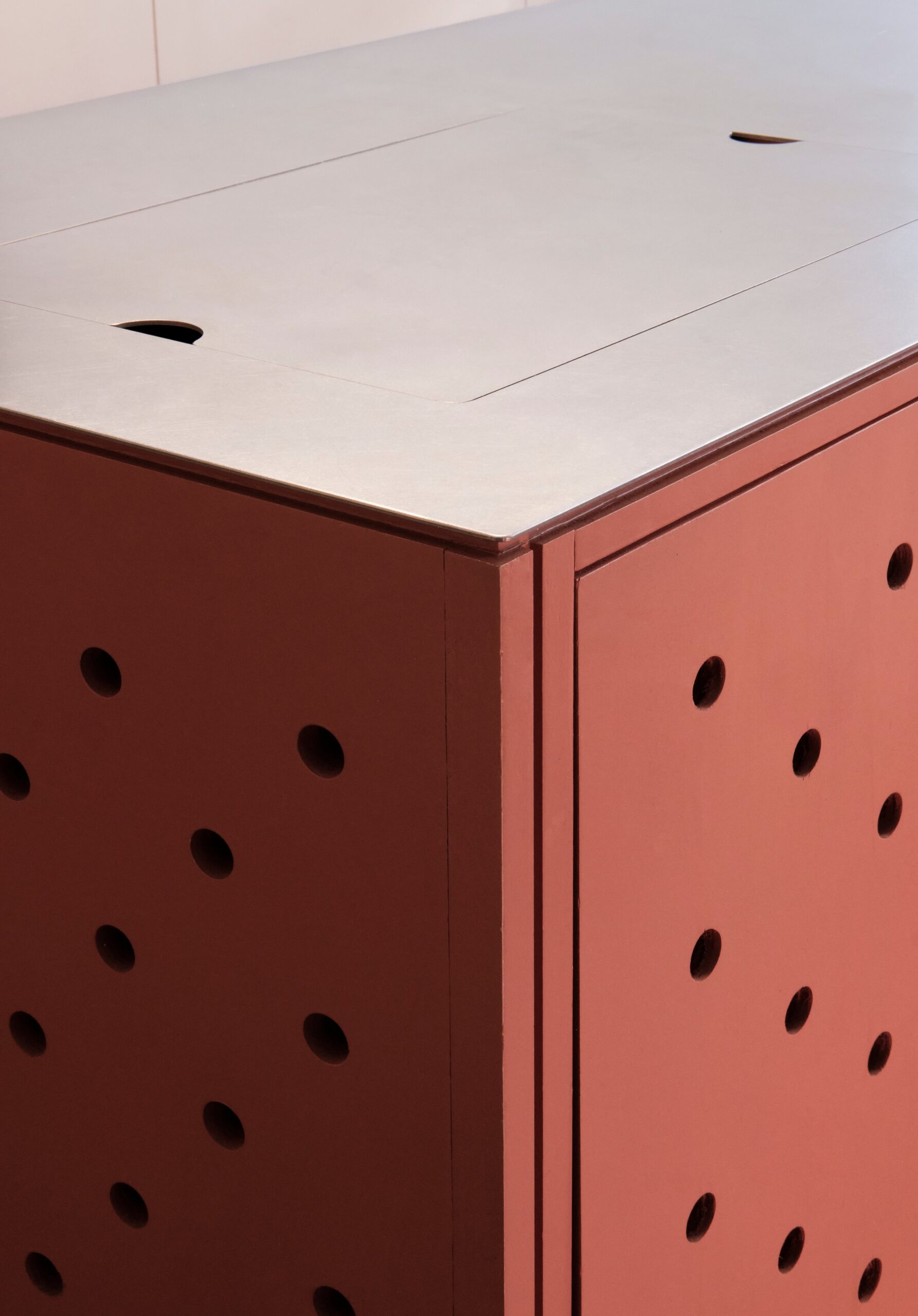 Close-up of a pale countertop above coral cabinet doors with circular openings.