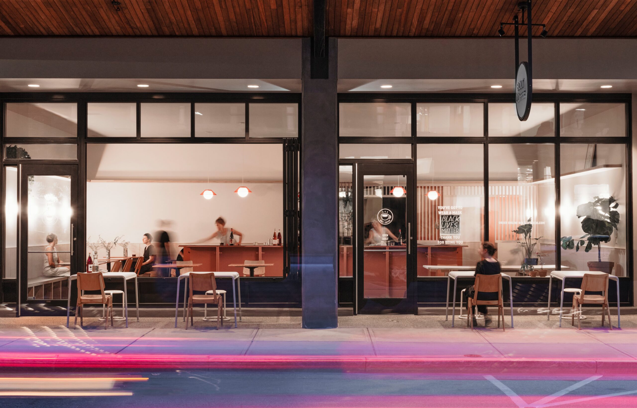 An illuminated café interior is visible through tall storefront windows at dusk.