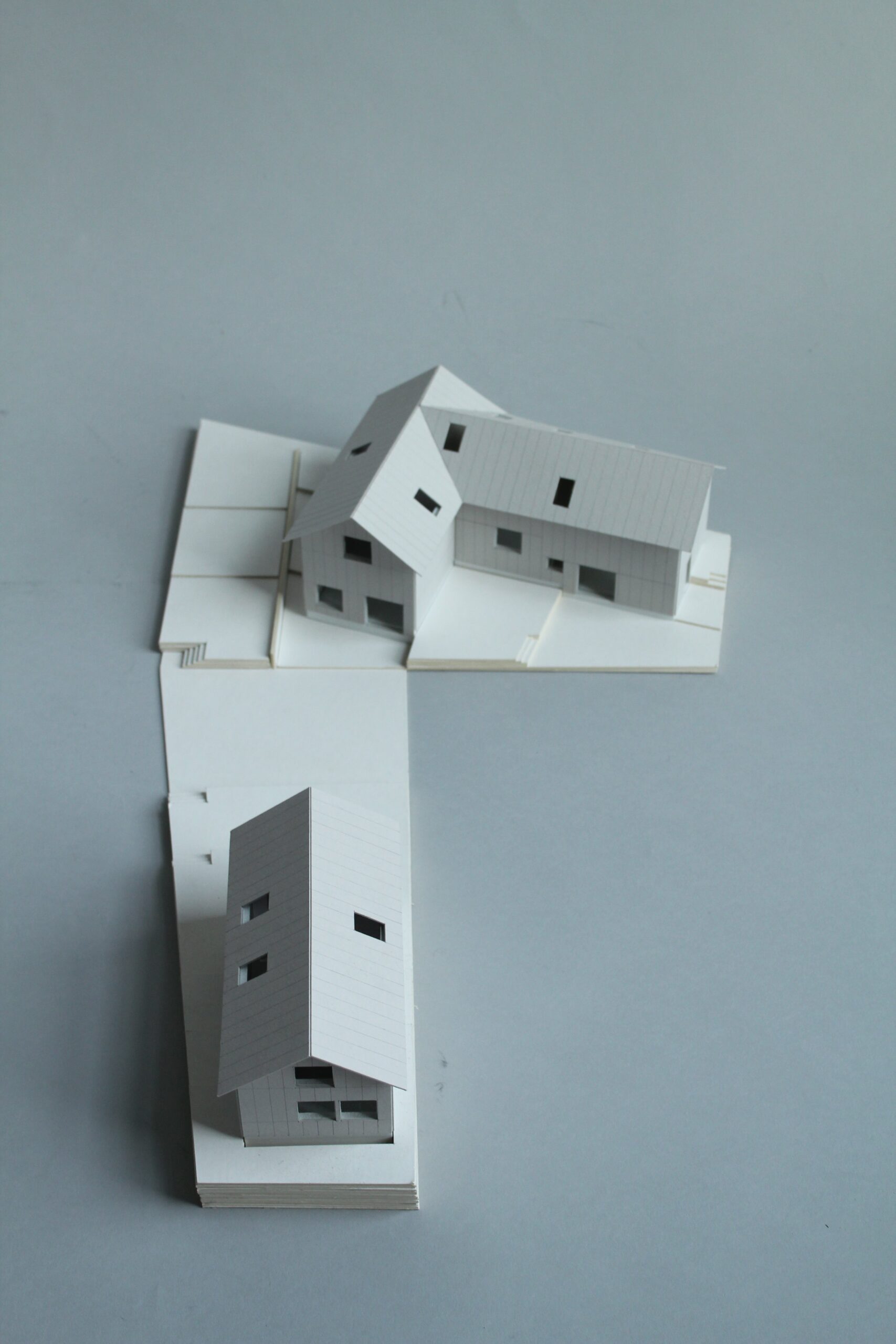 Overhead view of two white pitched-roof building models arranged on adjoining site bases.