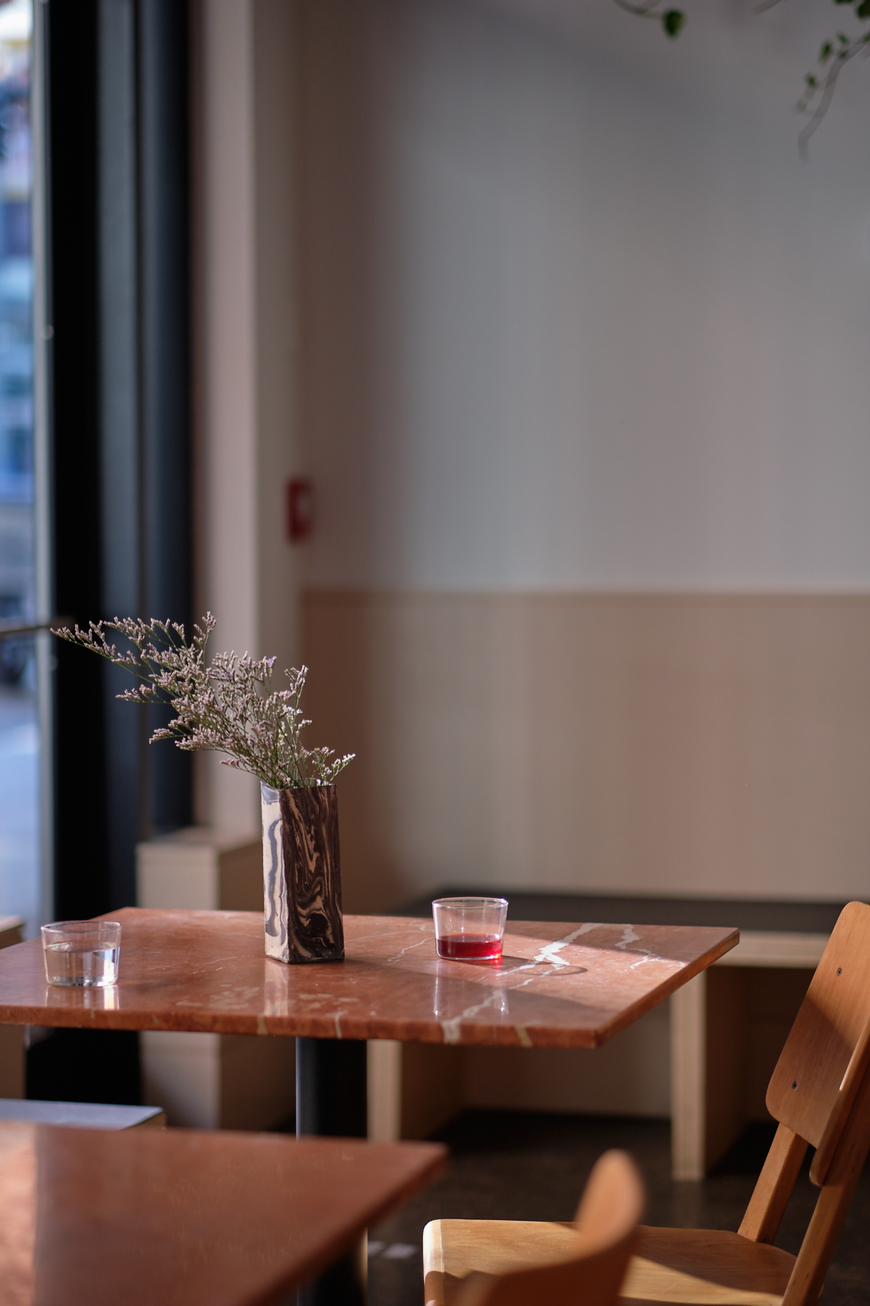 A wooden café table holds a vase and glasses beside a large street-facing window.