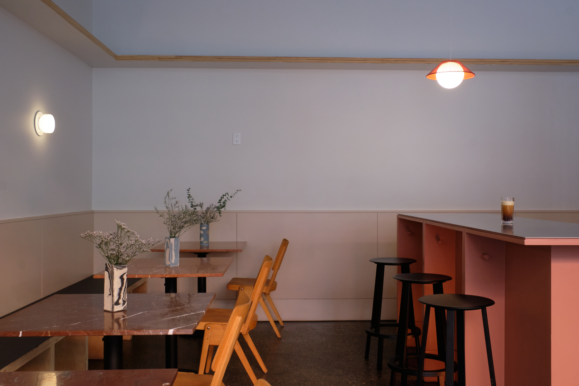 Wooden tables and chairs sit beside a coral counter beneath red-and-white pendant lights.