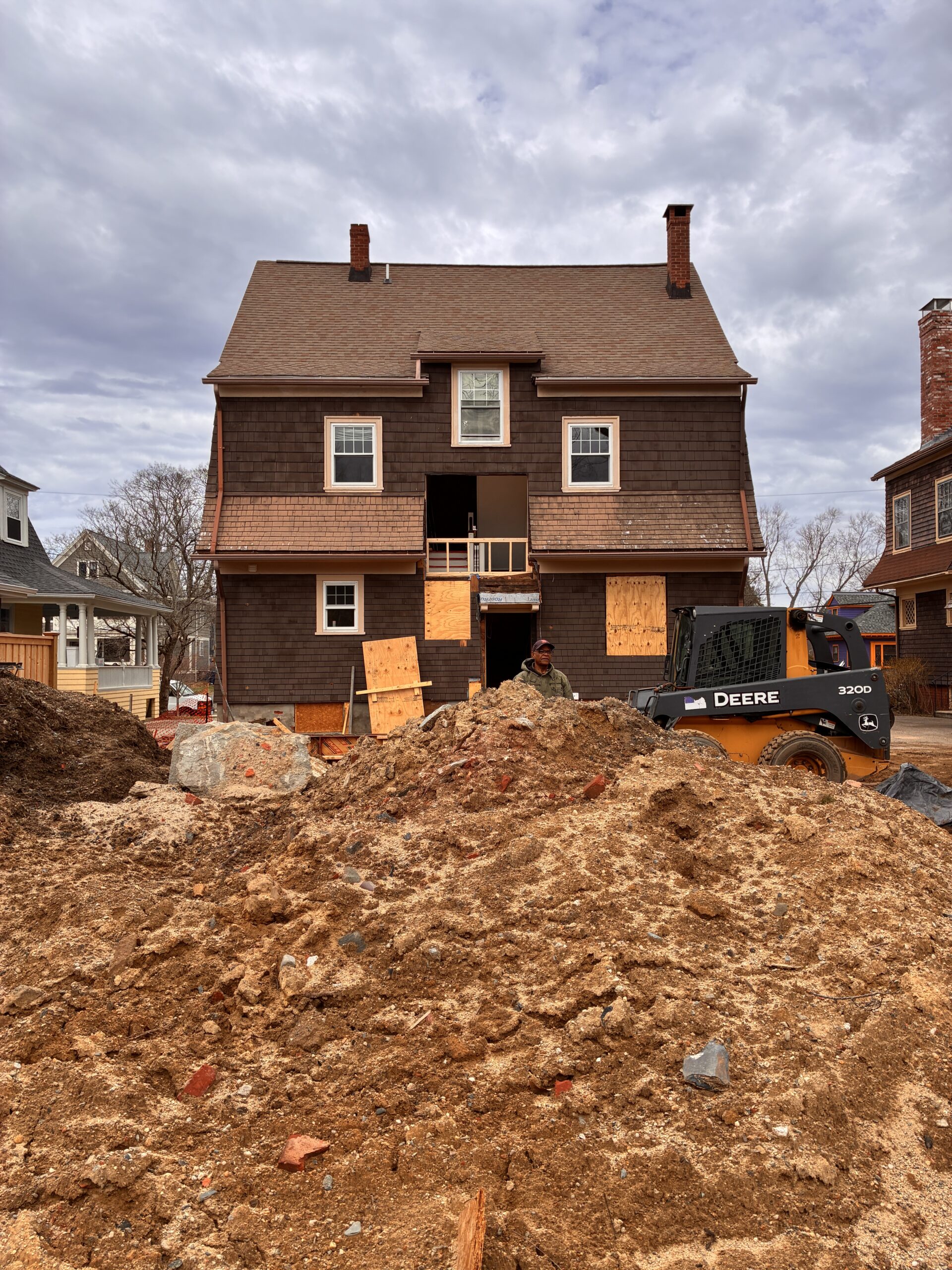 Excavated ground and construction equipment behind the existing two-story house.