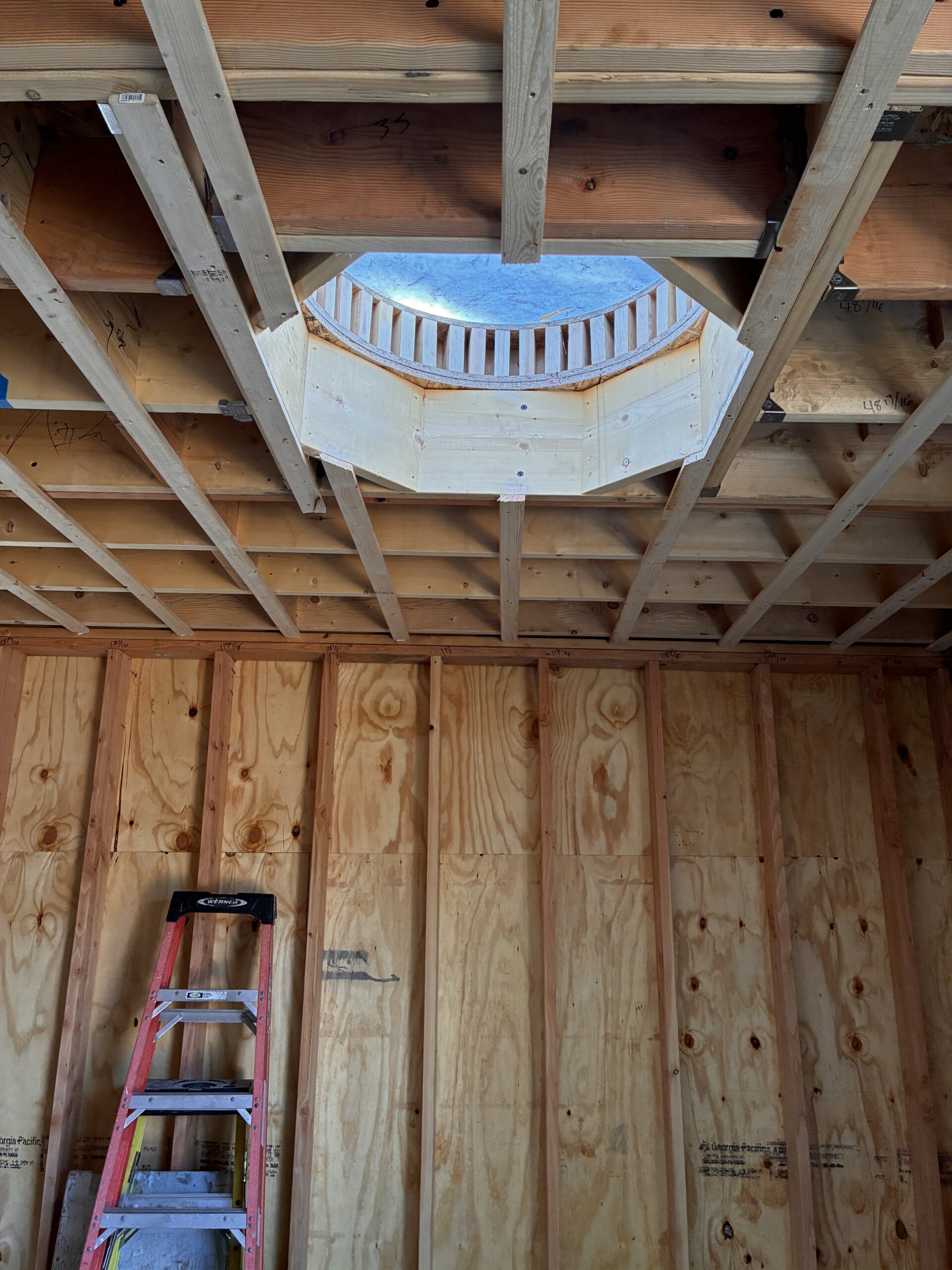 Exposed timber ceiling framing surrounds a circular skylight opening during construction.