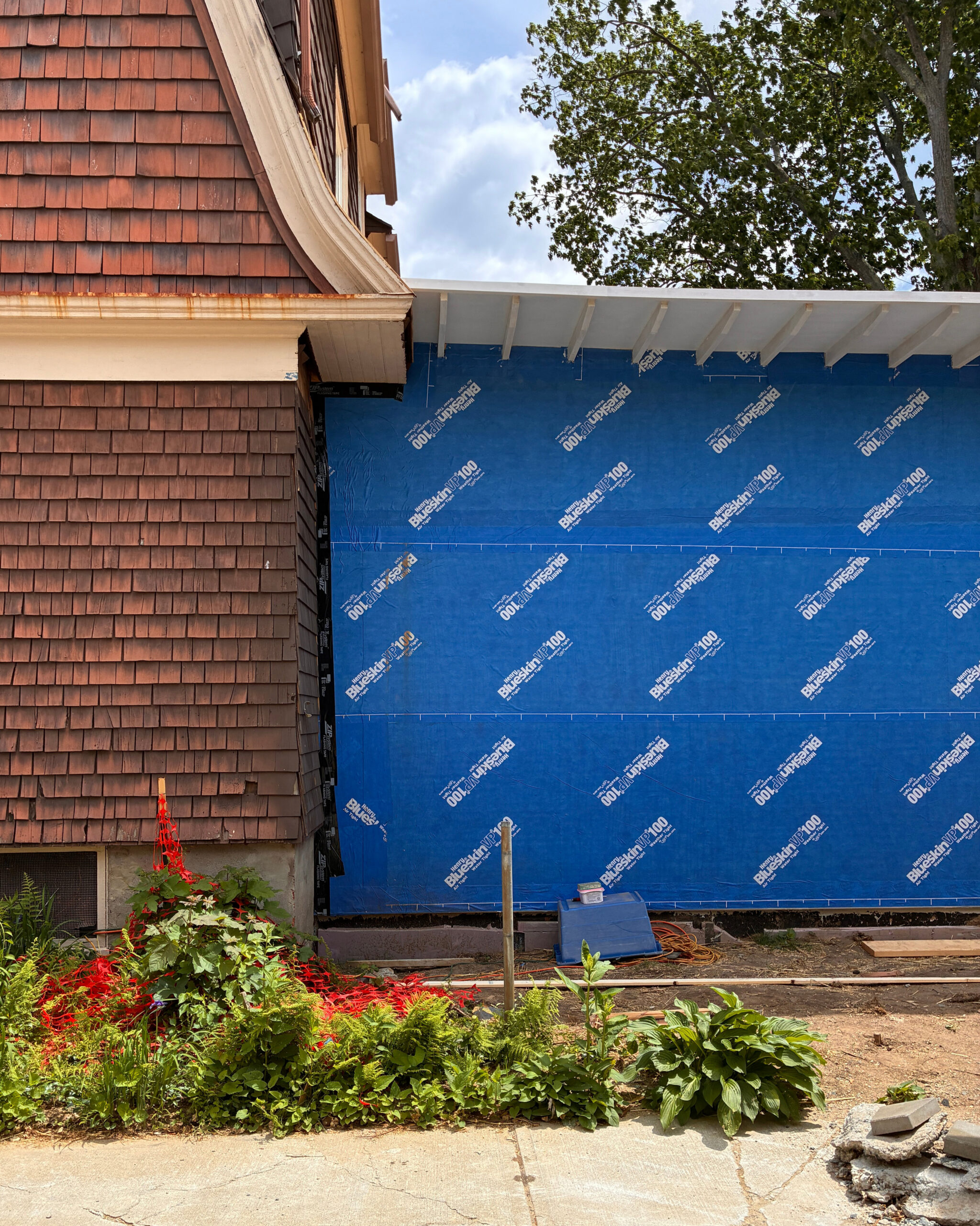 Blue-sheathed addition wall and exposed roof framing meet the existing shingled house.