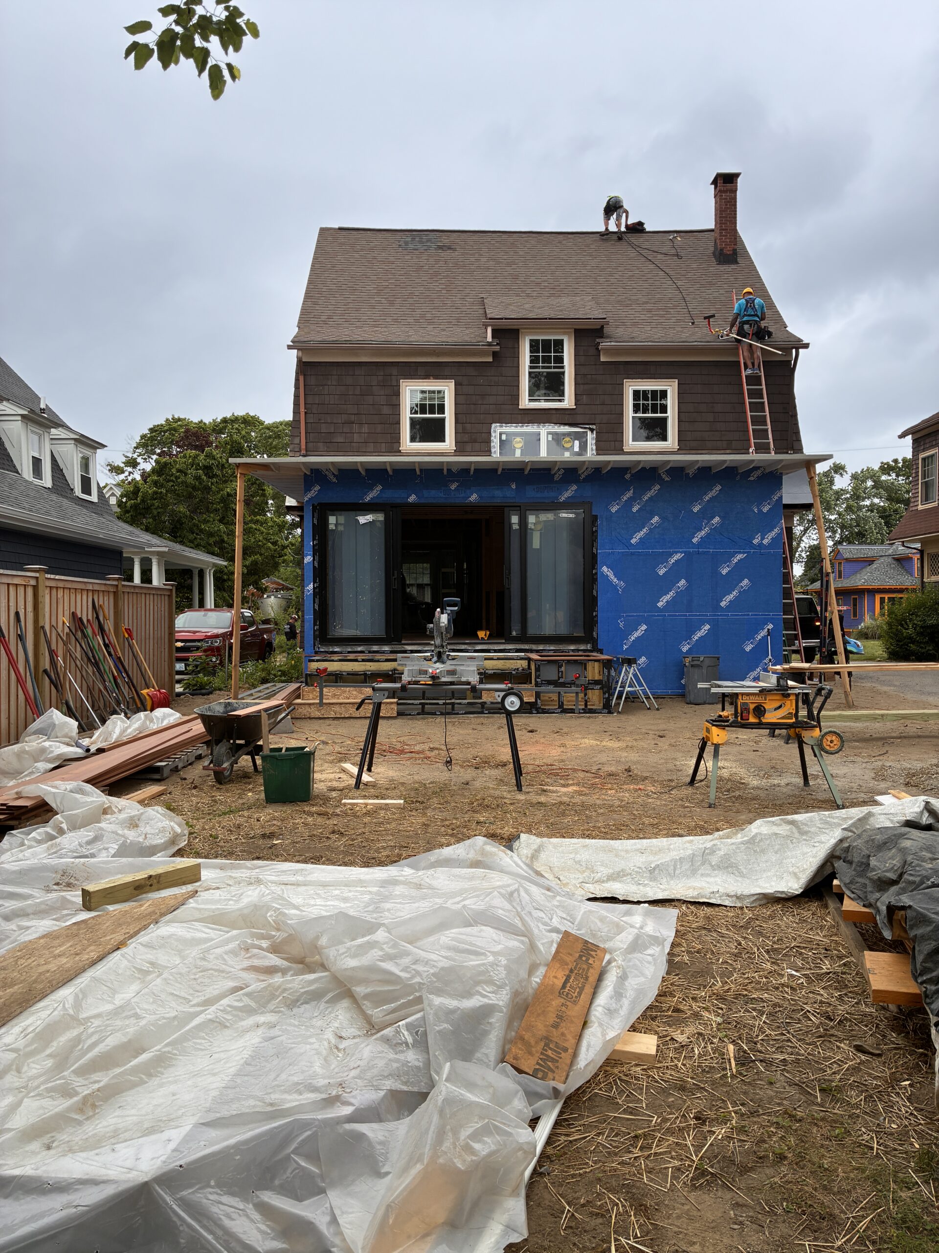 Rear view of the house and blue-sheathed addition with construction materials in the garden.